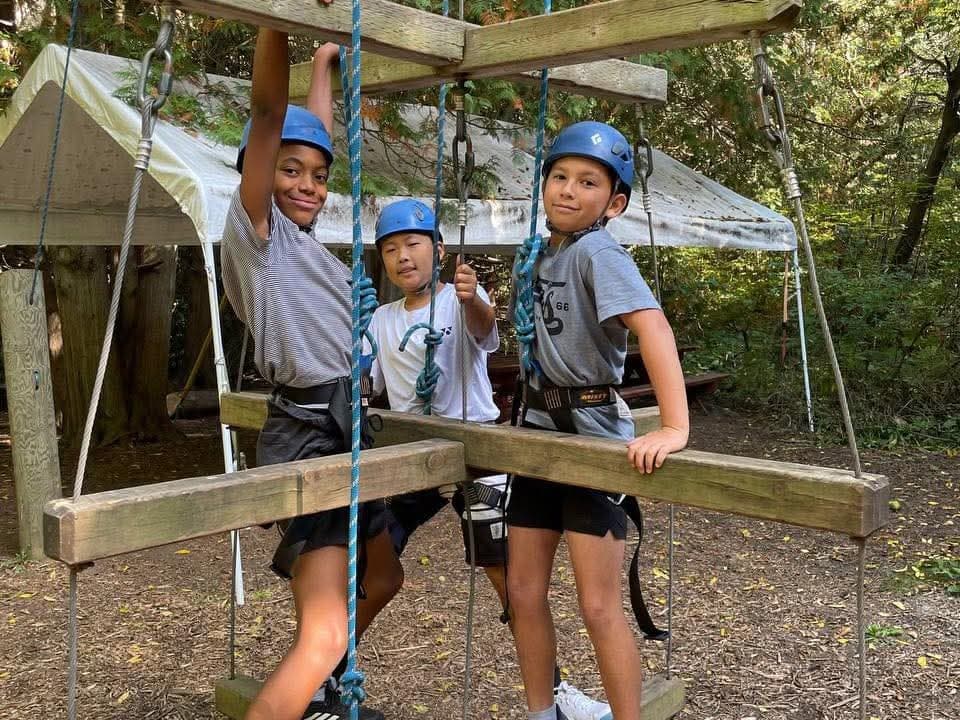 Three boys in blue helmets on a ropes adventure course in the woods