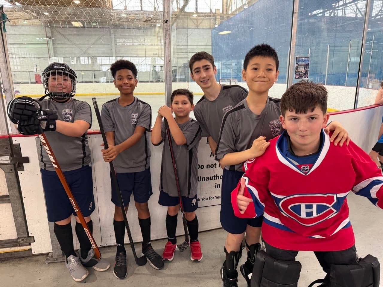Boys at a hockey arena with sticks, smiling with teammates