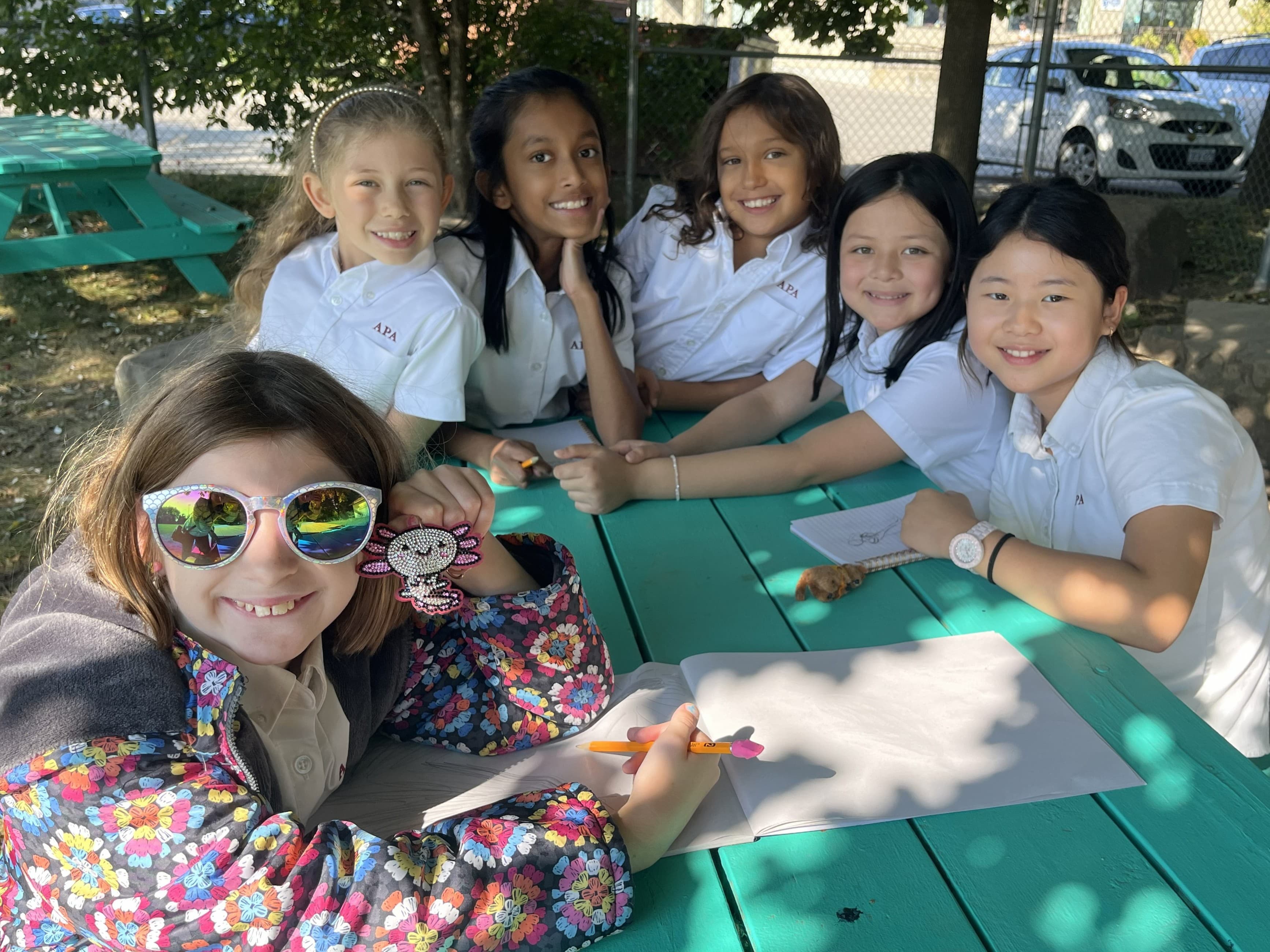 APA students gathered at a sunny outdoor picnic table, smiling together